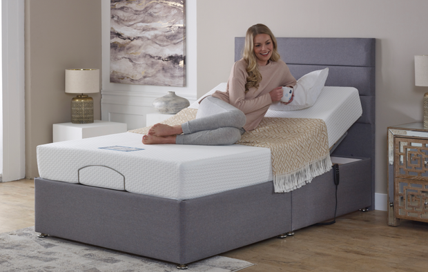 A woman relaxes on an adjustable bed, comfortably seated with a pillow behind her.