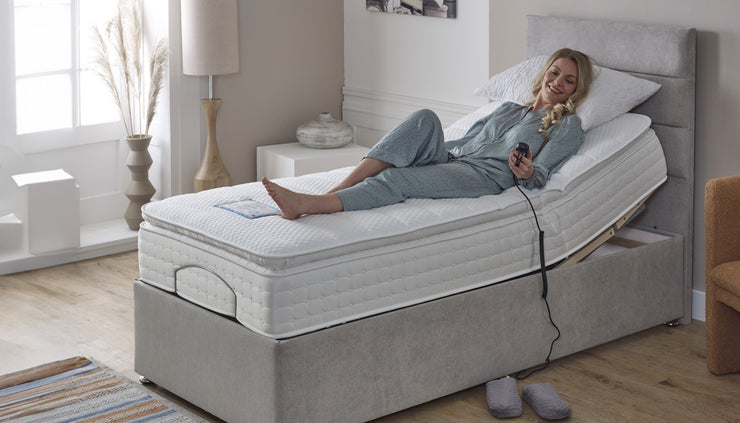 A woman relaxes on an adjustable bed, sitting comfortably on a mattress in a cozy bedroom setting.